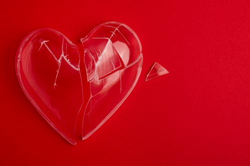 Cuore di plastica incrinato su sfondo rosso